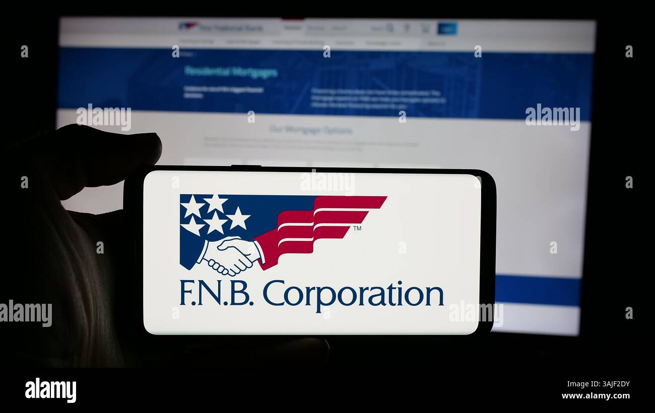Dans cette illustration photo, un téléphone portable avec le logo de la société américaine FNB Corporation (First National Bank) est vu sur l'écran en face de la page Web. Banque D'Images