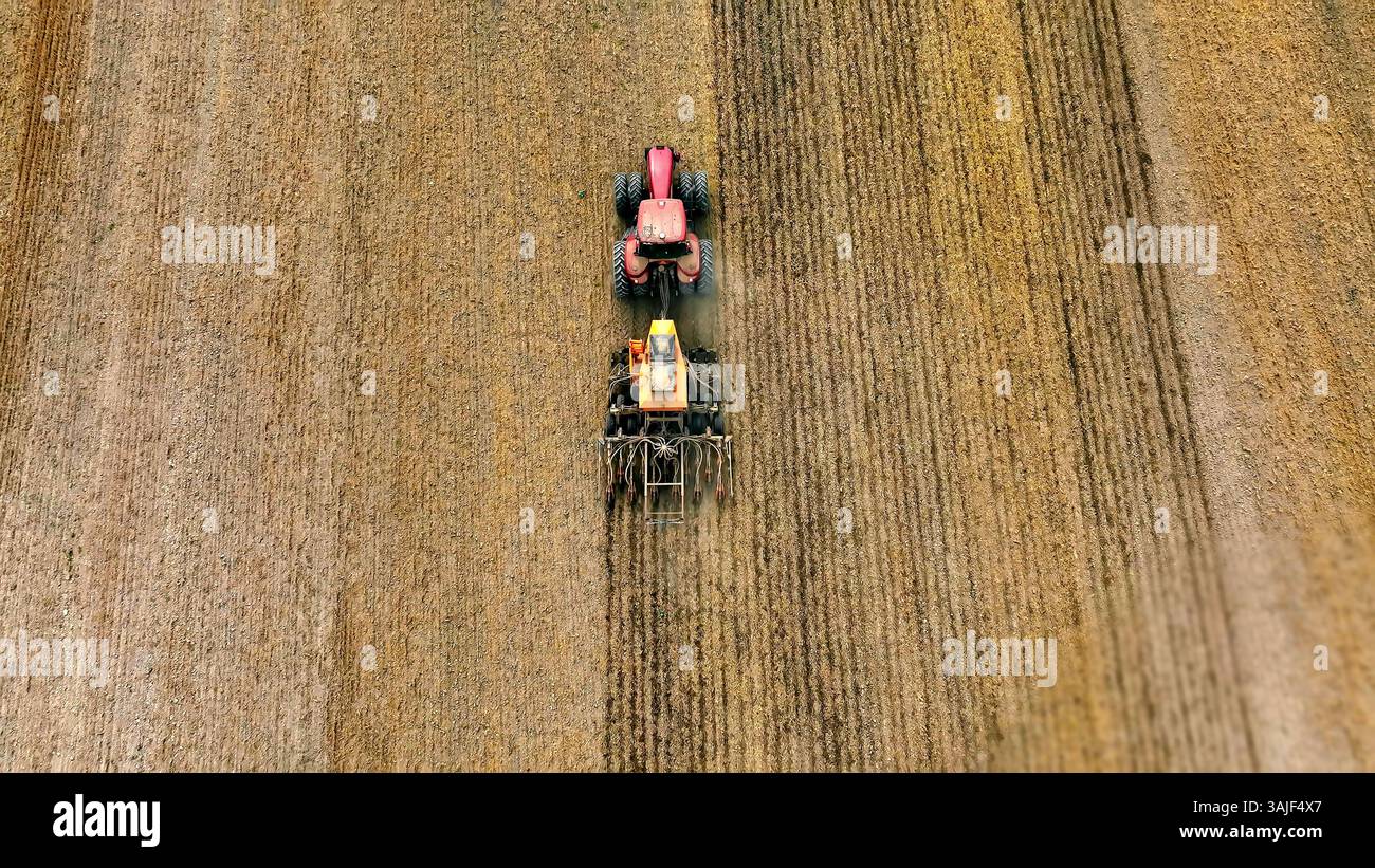 Tracteur labourant un champ par le dessus. Vue aérienne d'un tracteur rouge travaillant dans un champ sec, montrant le processus agricole de labourage et de préparation Banque D'Images