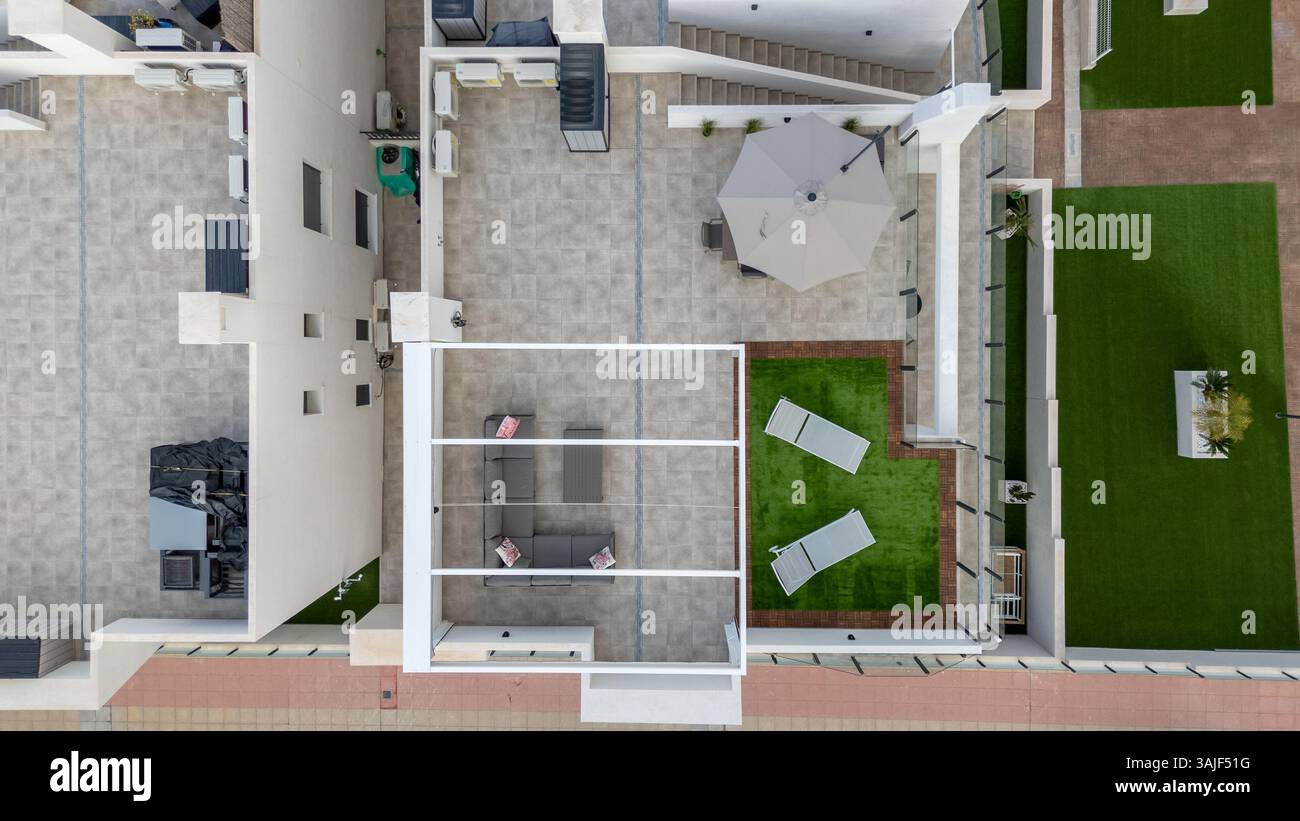 Prise de vue par drone d'un toit avec sièges modulaires, table, parasol et pelouse artificielle avec chaises longues dans un complexe d'appartements moderne. Banque D'Images