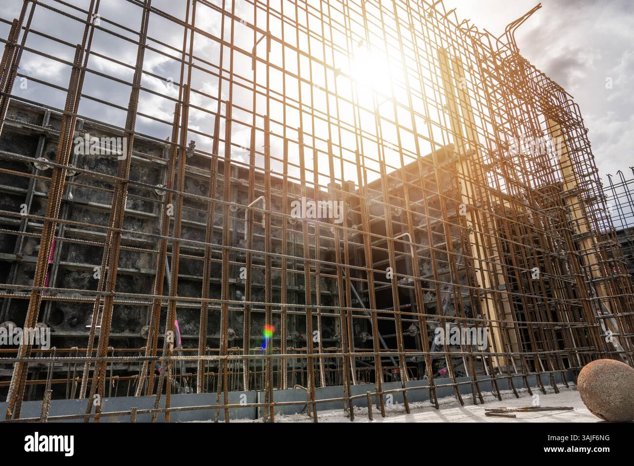 L'ossature en acier se tient haute sur un chantier de construction alors que la lumière du soleil brille à travers les barres. Les travailleurs peuvent être vus en arrière-plan se préparant pour le p suivant Banque D'Images