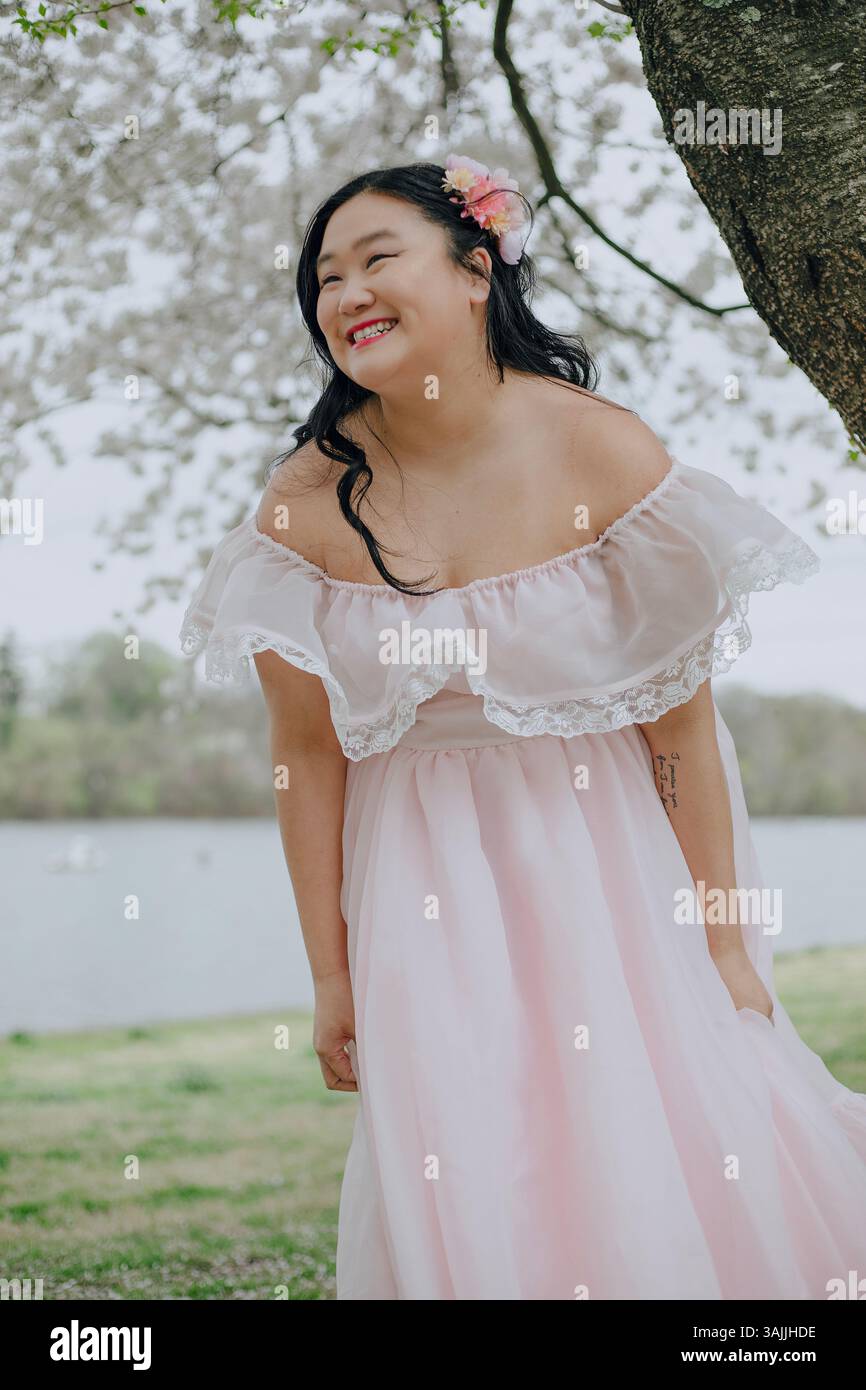 Femme asiatique aux cheveux longs portant une robe longue rose sur fond de fleurs de cerisier à Philadelphie, Pennsylvanie, États-Unis Banque D'Images