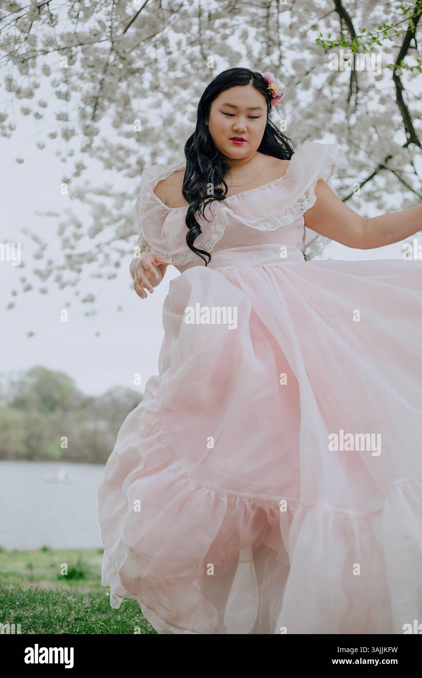Femme asiatique aux cheveux longs portant une robe longue rose sur fond de fleurs de cerisier à Philadelphie, Pennsylvanie, États-Unis Banque D'Images