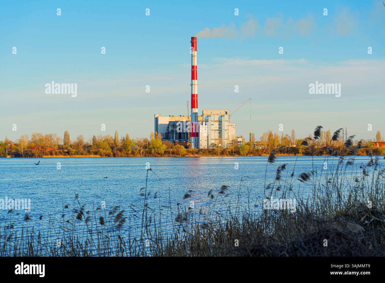 Installation d'incinération des déchets par un plan d'eau calme pendant la journée, mettant en évidence son architecture industrielle et son impact environnemental. Banque D'Images