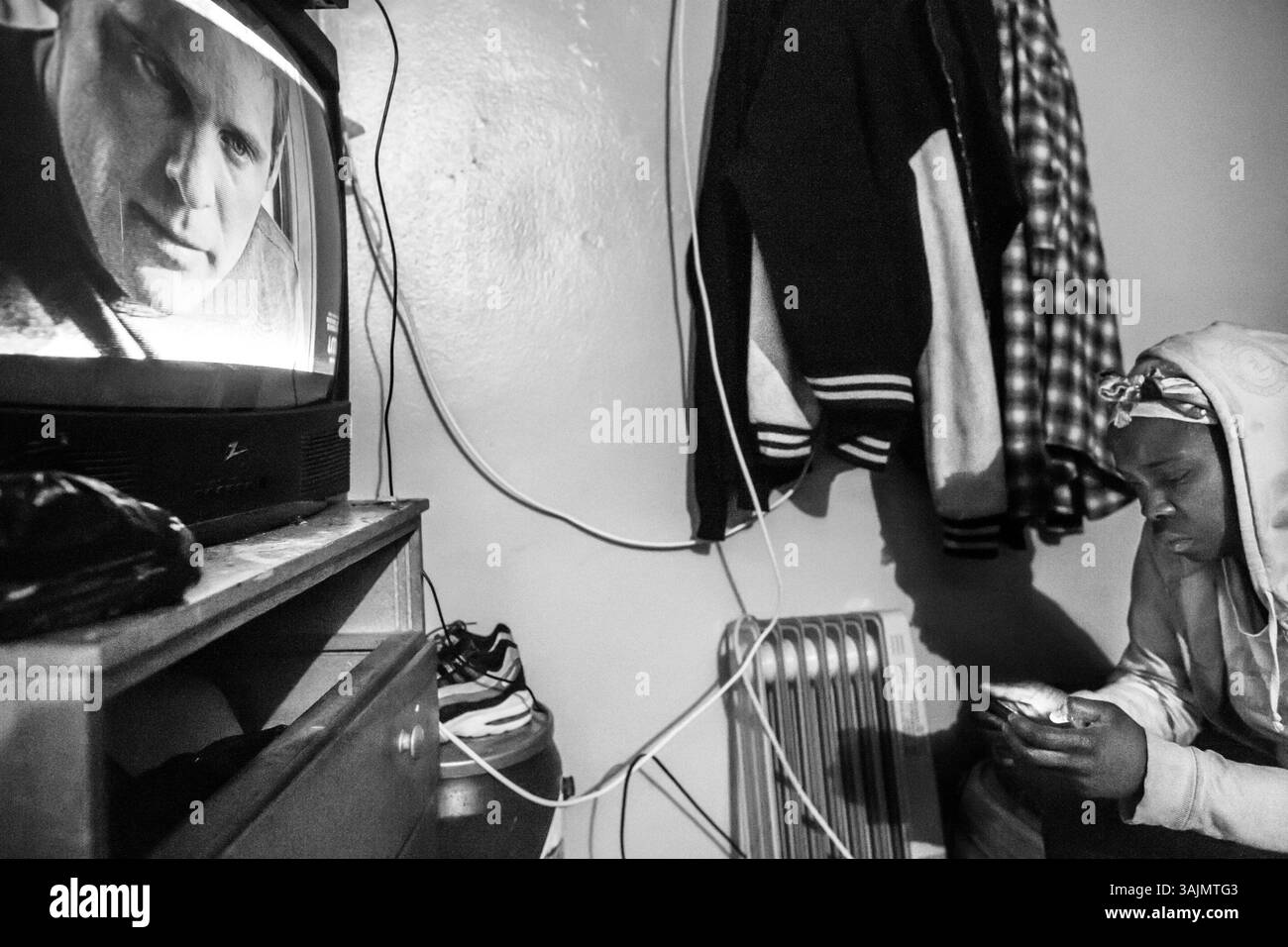 16 avril 2014 - Brooklyn, New York, États-Unis - Karen, mère de Kirell et tante de Smokey regarde son téléphone avec la télévision à l'intérieur de son appartement à Brooklyn. La toute-puissante Nation latine Roi et Reine (ALKQN, ALKN, LKN) est le plus ancien et le plus grand gang de rue hispanique des États-Unis. Ses racines datent de 1954 Humboldt Park à Chicago, Illinois. (Crédit image : © Nicolas Enriquez/ZUMA Wire/ZUMAPRESS.com) Banque D'Images