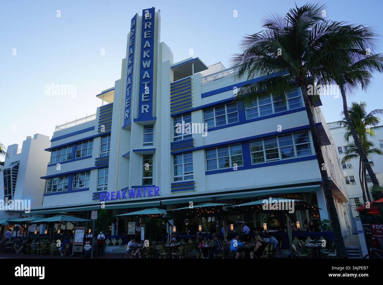 Les touristes s'assoient dans un bar en face de l'historique Breakwater Hotel dans le quartier emblématique de Miami Art déco à Miami Beach. Banque D'Images