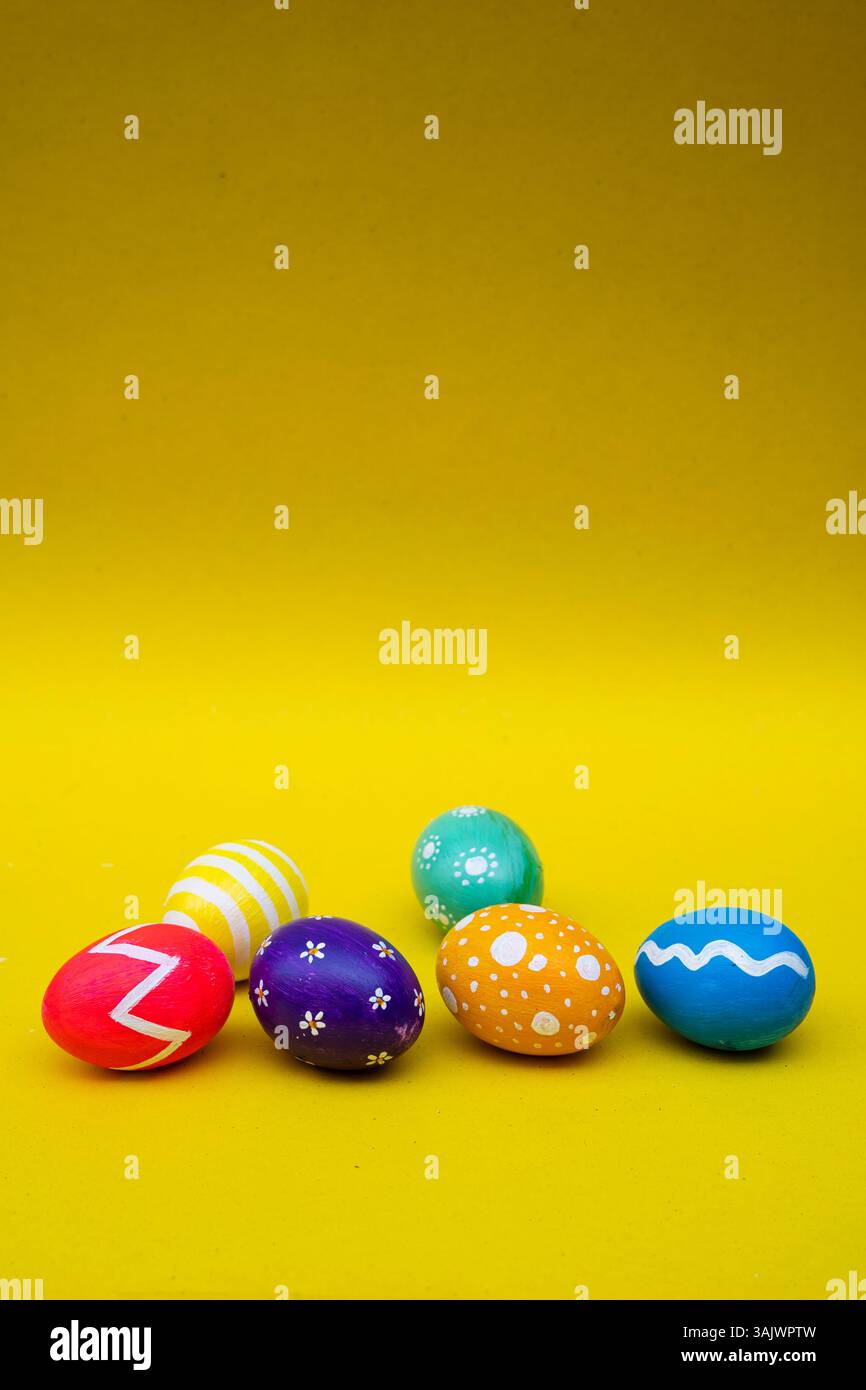 Beaux oeufs peints à la main en violet, jaune, bleu, vert, rouge, et orange disposé sur une surface jaune pour les célébrations de Pâques. Banque D'Images