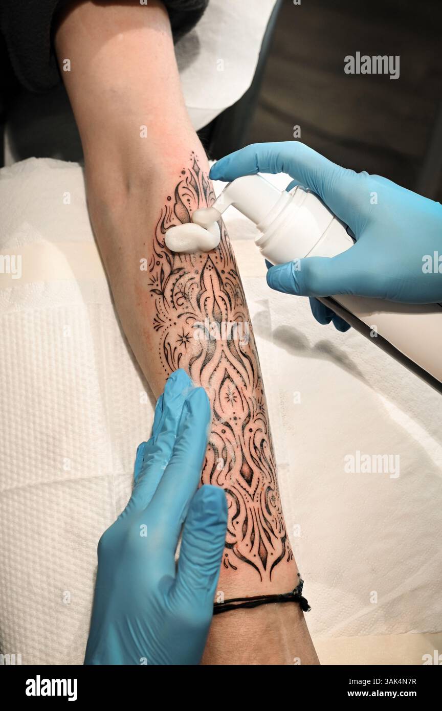 Tatoueur étalant la crème hydratante sur l'avant-bras d'un client avec un tatouage ornemental frais Banque D'Images