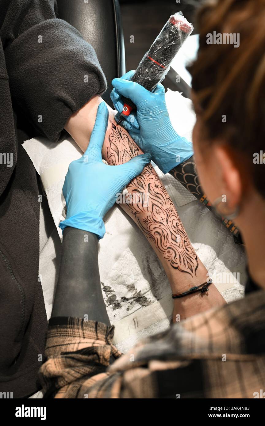Tatoueur dessinant soigneusement un tatouage à l'encre noire sur le bras d'un client, créant l'art corporel permanent Banque D'Images