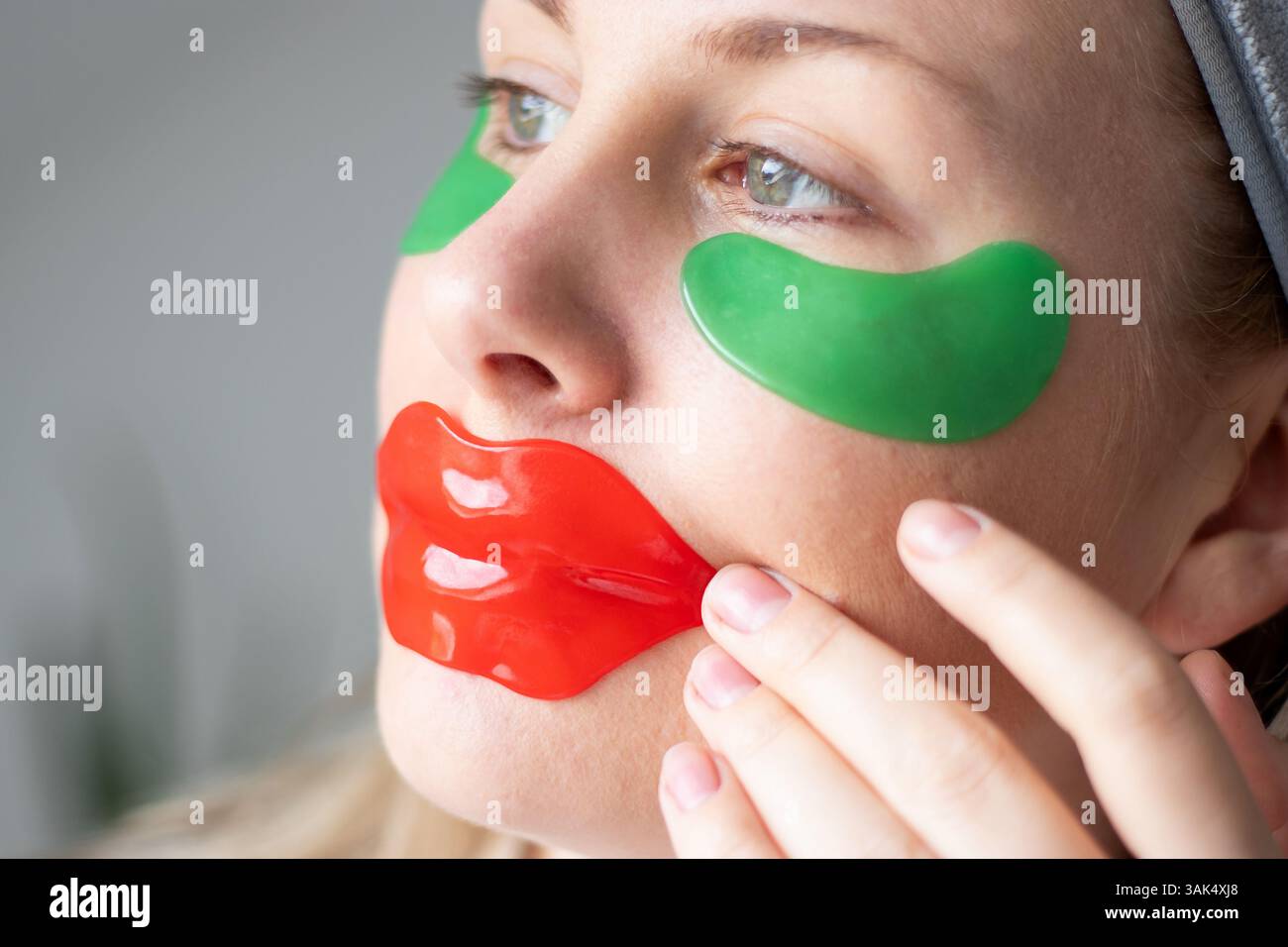 Gros plan d'une femme caucasienne utilisant un masque à lèvres en gel de collagène rouge et des patchs de gel pour les yeux verts sous ses yeux Banque D'Images