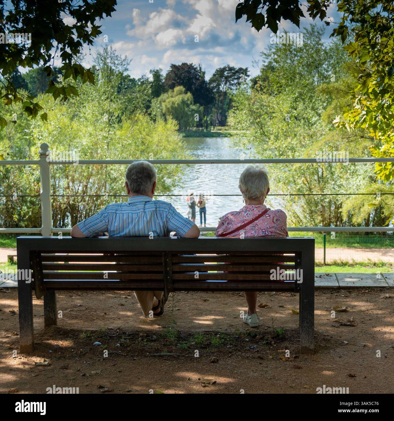 Vichy. Deux personnes âgées sont assises sur un banc, regardant la rivière Allier, tandis qu'un jeune couple capture des souvenirs à proximité. Allier. Auvergne . France Banque D'Images