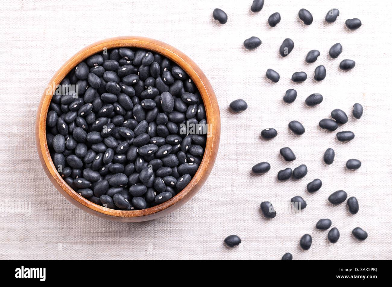 Haricots noirs dans un bol en bois sur lin. Variété séchée de haricots communs, Phaseolus vulgaris, également connu sous le nom de haricots de tortue noire, et caviar criollo. Banque D'Images