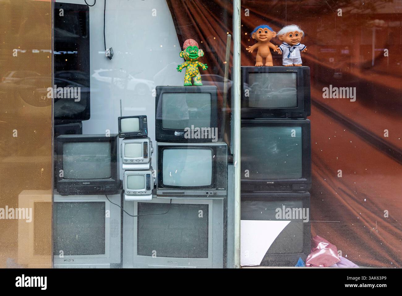 Tel Aviv-Jaffa, Israël. 9 avril 2025, Une vitrine montrant une pile de vieux téléviseurs à tube cathodique avec des poupées troll vintage sur le dessus, reflectin Banque D'Images