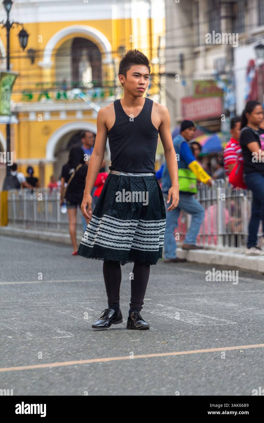 Un mannequin masculin portant une jupe marche en toute confiance dans une rue de la ville d'Iloilo lors d'un défilé de mode en plein air organisé dans un cadre urbain public Banque D'Images