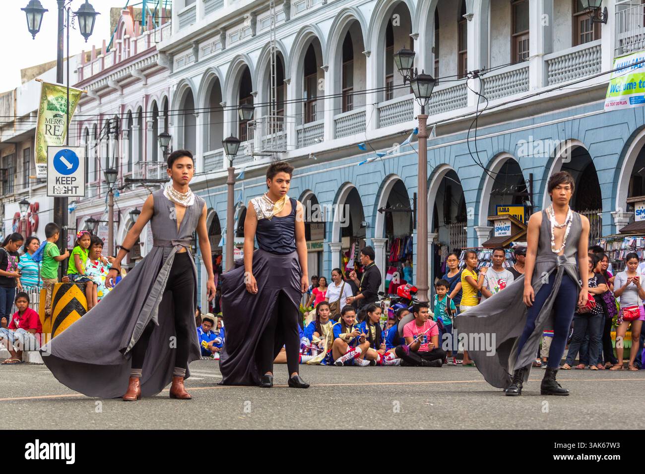 Les mannequins masculins portant une jupe marchent en toute confiance dans une rue de la ville d'Iloilo lors d'un défilé de mode en plein air tenu dans un cadre urbain public Banque D'Images