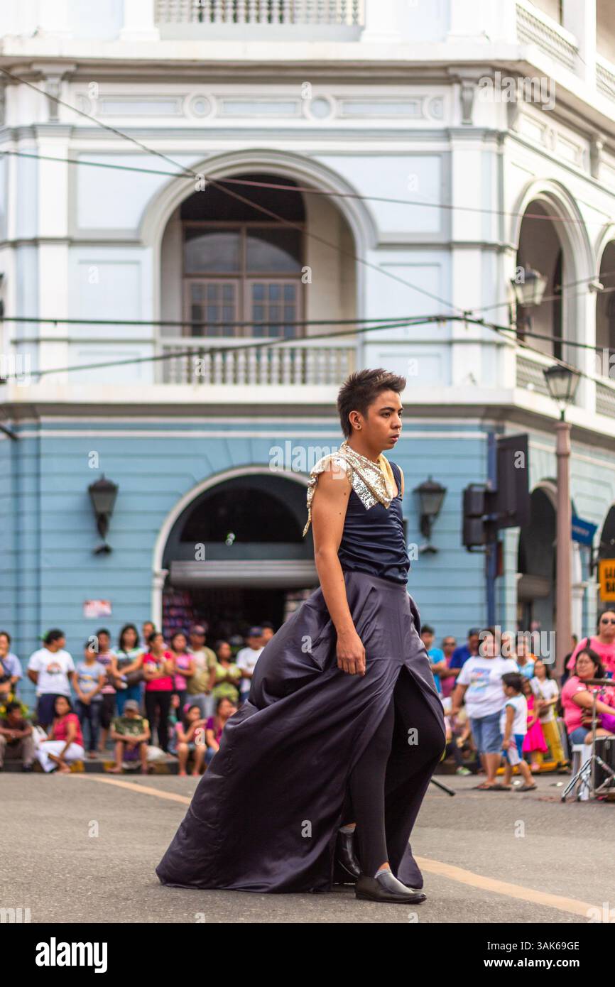 Un mannequin masculin portant une jupe marche en toute confiance dans une rue de la ville d'Iloilo lors d'un défilé de mode en plein air organisé dans un cadre urbain public Banque D'Images