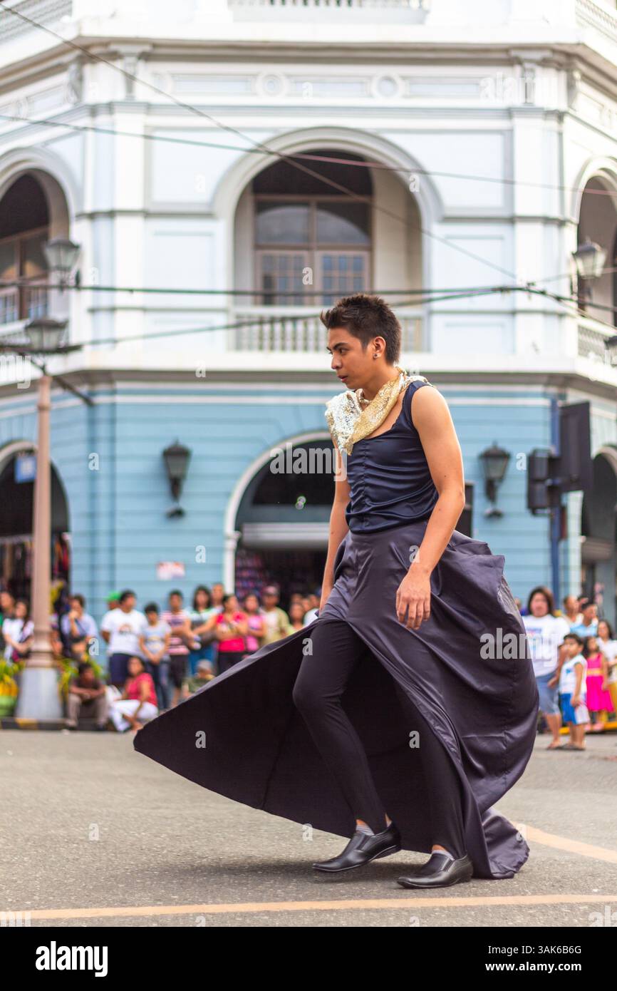 Un mannequin masculin portant une jupe marche en toute confiance dans une rue de la ville d'Iloilo lors d'un défilé de mode en plein air organisé dans un cadre urbain public Banque D'Images