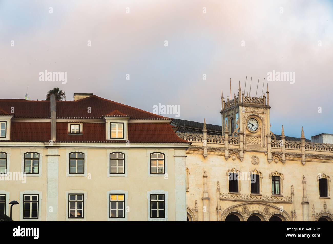 La façade ornée de la gare Rossio de Lisbonne, avec son architecture néo-manuéline et sa tour de l'horloge, se dresse contre un ciel pastel au lever du soleil, en hauteur Banque D'Images