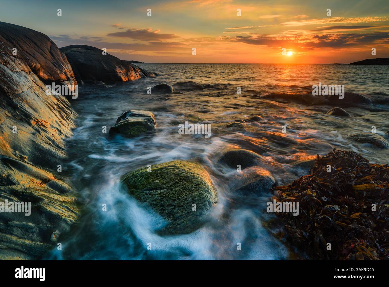 Cette vue magnifique sur la côte capture le coucher de soleil sur la mer Baltique en Suède. Les vagues tapent doucement contre les rochers, créant une atmosphère sereine avec wa Banque D'Images