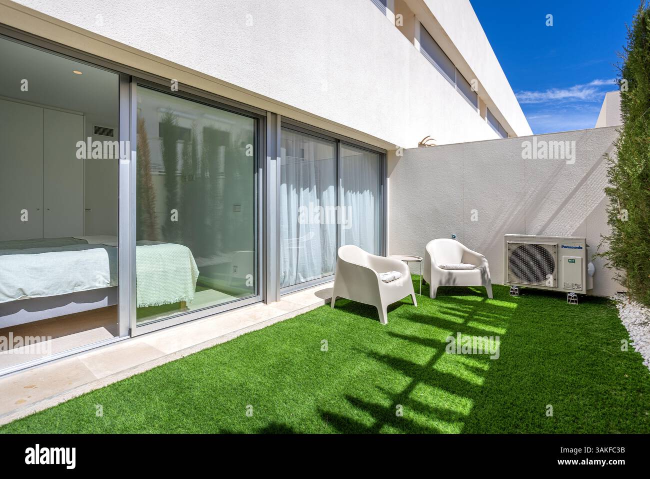 Terrasse de jardin privée confortable à l'extérieur de la chambre avec gazon artificiel, deux chaises et des murs d'intimité ombragés. Banque D'Images