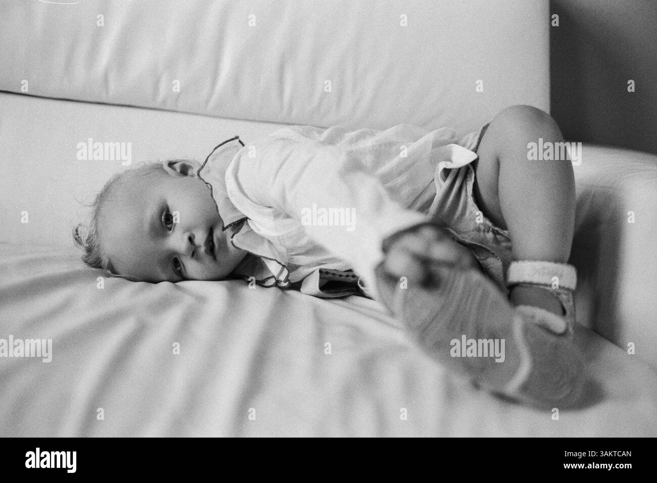 Une petite fille, vêtue de franges, couchée sur un canapé et regardant directement l'appareil photo Banque D'Images