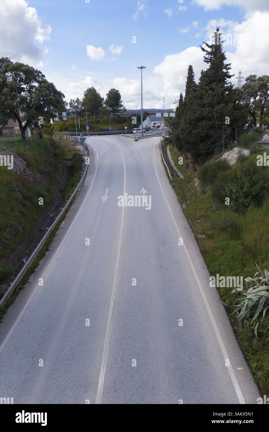 Vue panoramique d'une route vide à deux voies s'étendant vers un rond-point, encadrée par des arbres et sous un ciel nuageux Banque D'Images