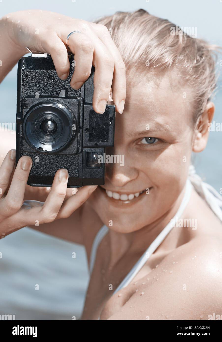 Femme en riant avec amusement qu'elle considère une photo sur l'arrière de l'appareil photo dans le viseur. Technicolor 70s retro style correction couleur Banque D'Images