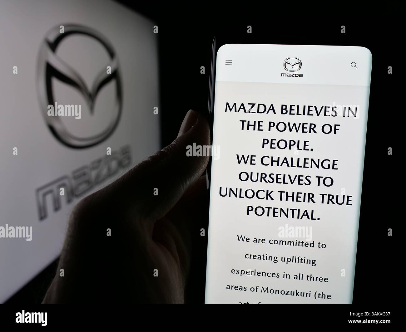 Stuttgart, Allemagne - 11-27-2024 : Personne tenant un téléphone portable avec la page Web de la société automobile japonaise Mazda Motor Corporation sur l'écran avec le logo. Banque D'Images