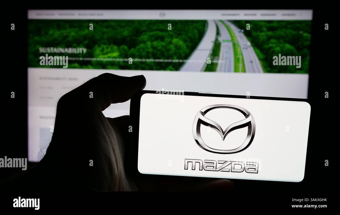 Stuttgart, Allemagne - 11-27-2024 : Personne tenant un téléphone portable avec le logo de la société automobile japonaise Mazda Motor Corporation sur l'écran Banque D'Images
