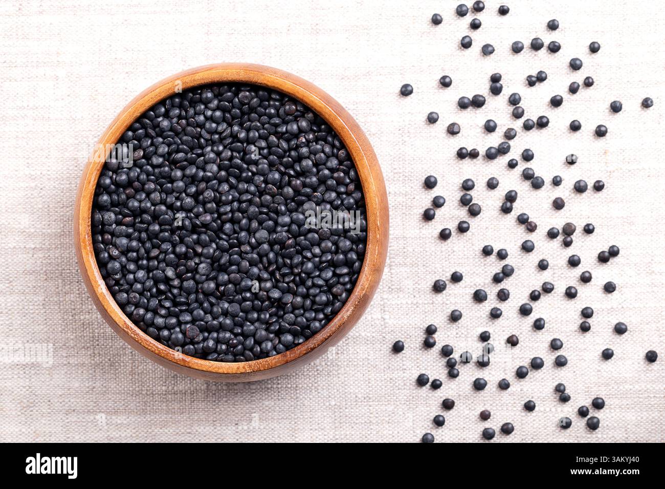 Lentilles béluga dans un bol en bois sur lin. Variété séchée d'une petite lentille noire, Lens esculenta, également connue sous le nom de lentilles de caviar. Banque D'Images