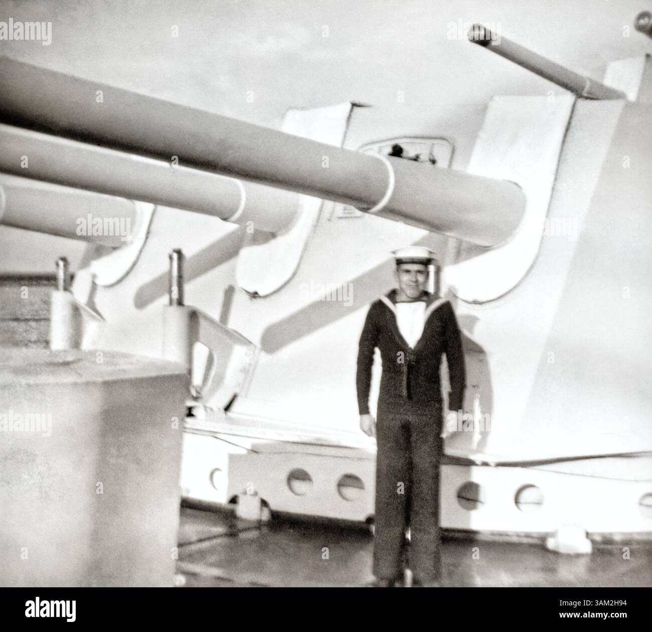 Marin de la Royal Navy posant devant une tourelle de canon d'un croiseur. Banque D'Images