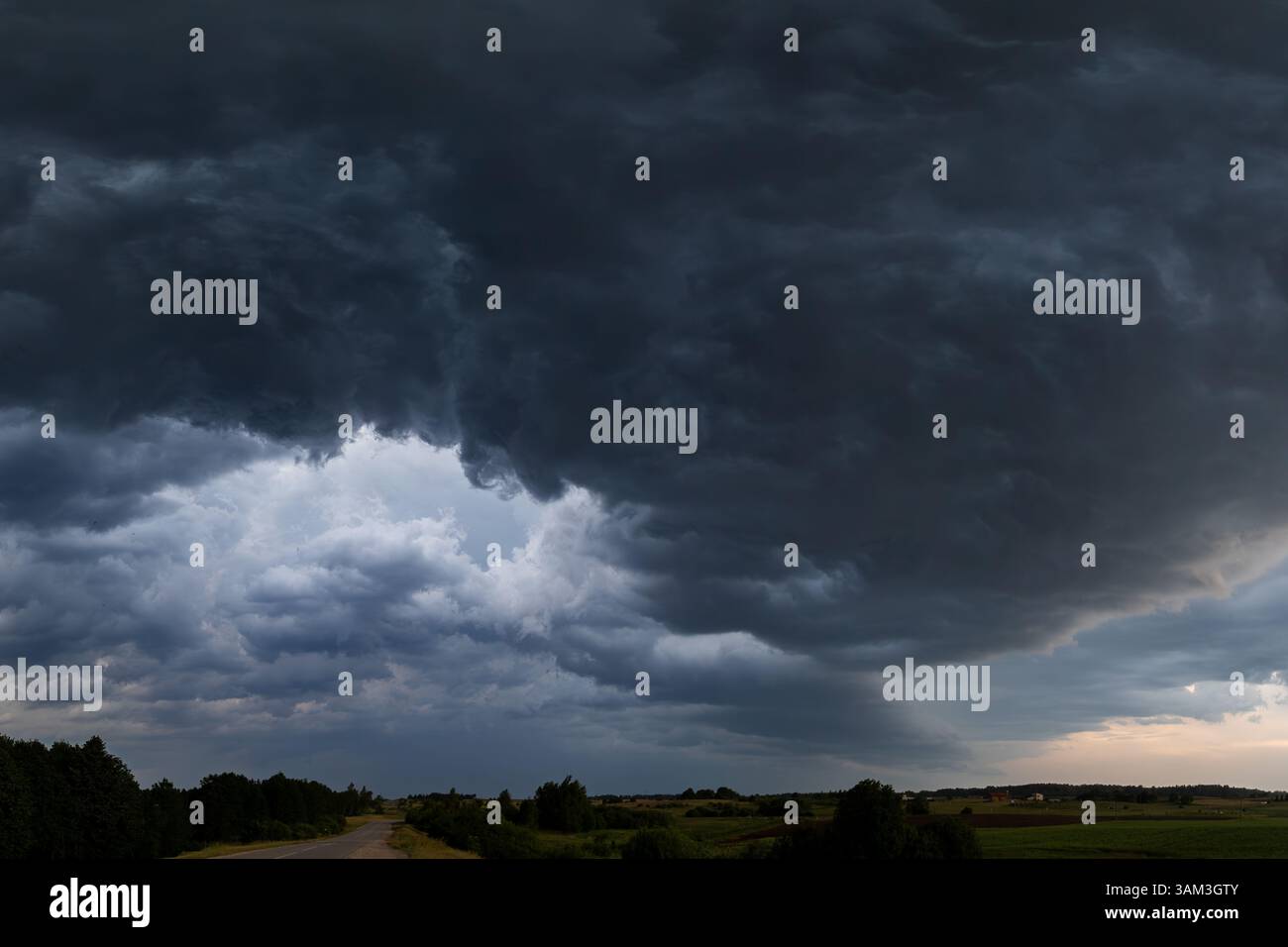 Une masse dramatique de nuages sombres descend sur une route tranquille de campagne en Lituanie. Les textures en couches des nuages transmettent l'intensité de t Banque D'Images