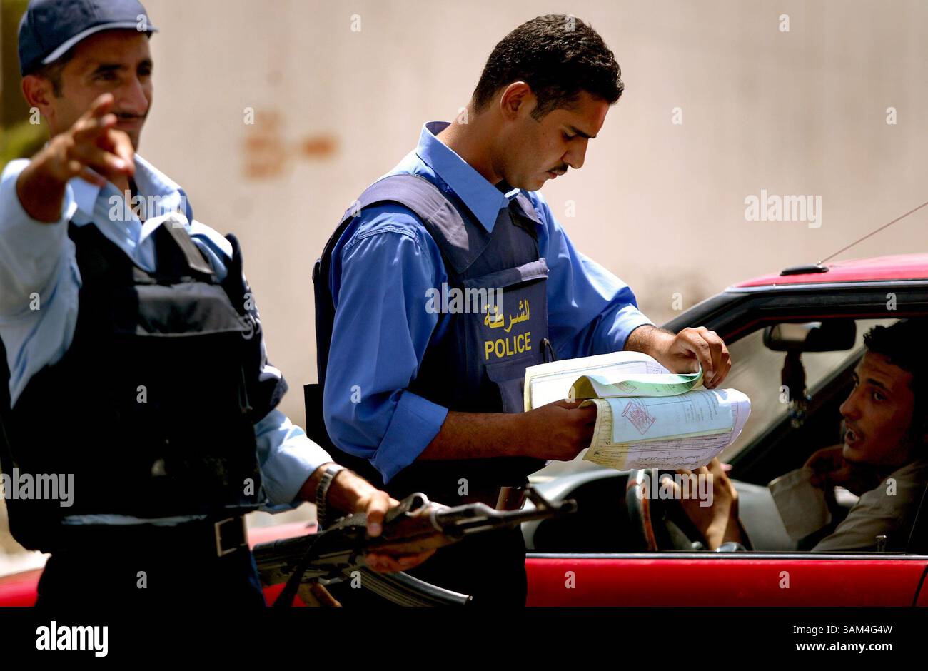 22 juin 2004 - États-Unis - un policier irakien passe en revue les documents d'un conducteur pour son véhicule à un poste de contrôle. À mesure que la date du transfert de pouvoir approche, la police a intensifié ses efforts et conduit davantage de points de contrôle. Récemment, ils ont reçu l'ordre de donner des citations pour des infractions au code de la route, une loi qui n'a pas été appliquée depuis le début de la guerre l'année dernière. Photo prise mardi 22 juin 2004..Star-Telegram/Khampha Bouaphanh (crédit image : © Khampha Bouaphanh/mct/ZUMAPRESS.com) Banque D'Images