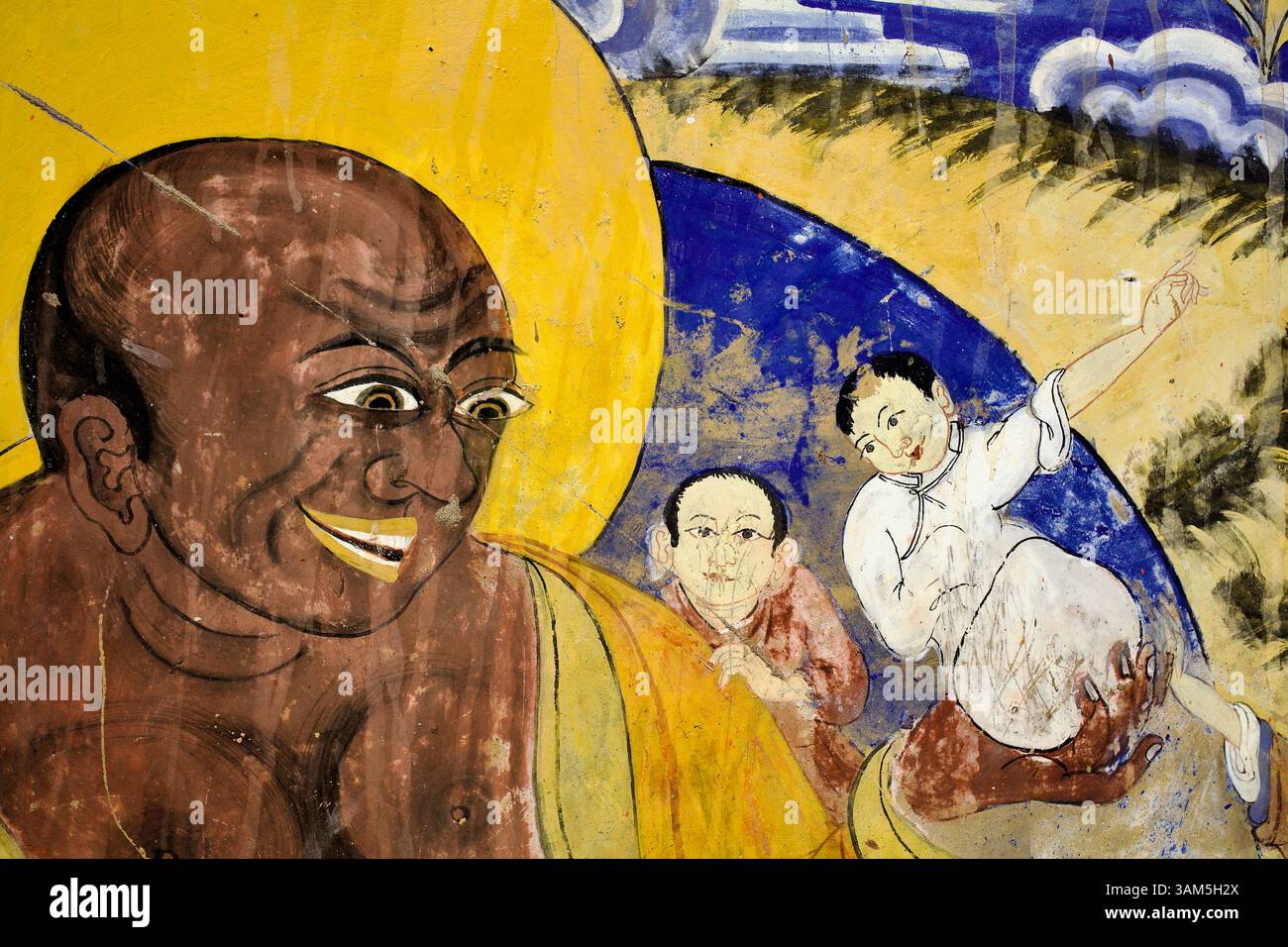 Détail mural d'un moine joyeux ou d'une figure de Budai berçant un enfant, symbolisant la compassion et l'abondance insouciante, monastère Thiksey, Ladakh. Banque D'Images