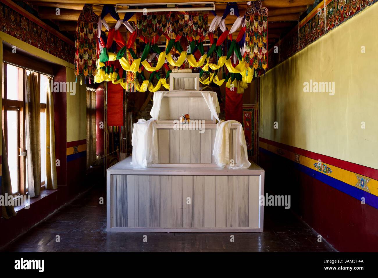 Base de stupa à étages blancs avec offrandes khata et canopée cérémonielle dans un couloir de la salle de prière principale, monastère Thiksey, Ladakh, Inde. Banque D'Images