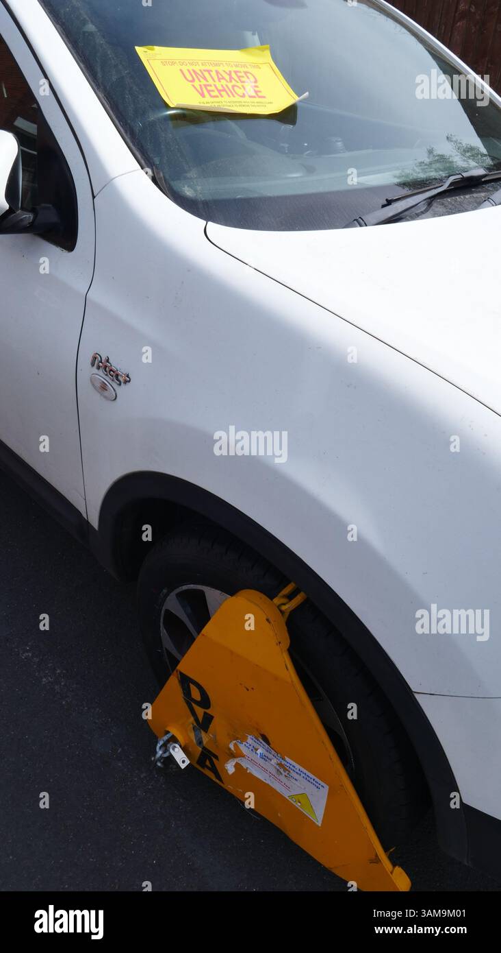 Un véhicule dans une rue latérale est fixé sur une roue et l'avis « véhicule non fixé » est apposé sur son pare-brise par l'Agence de permis de conduire et de véhicules (DVLA) Banque D'Images