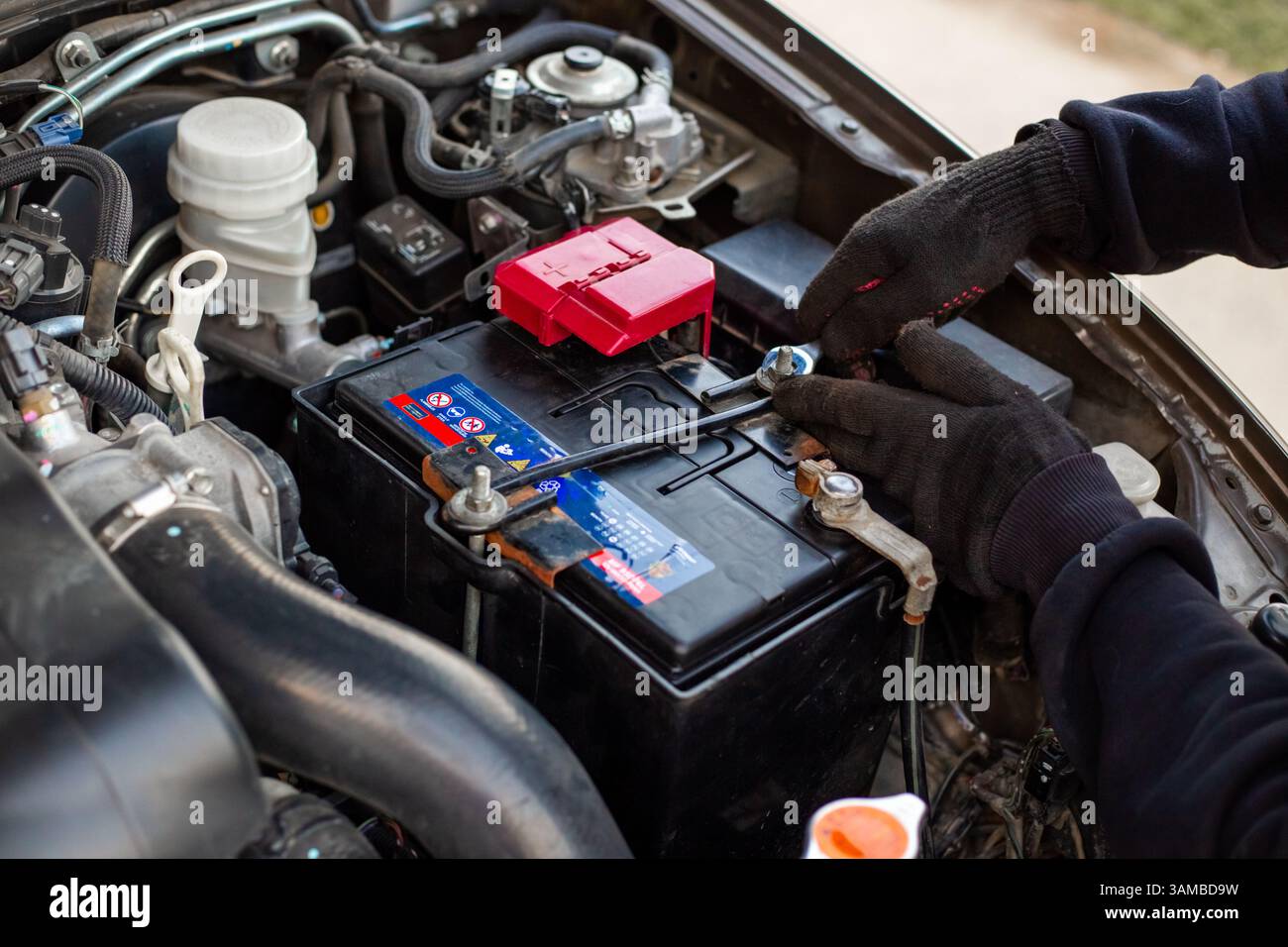 Remplacement de la batterie d'une voiture. Le mécanicien installe la batterie en fixant le support de montage de la batterie avec une clé. Banque D'Images