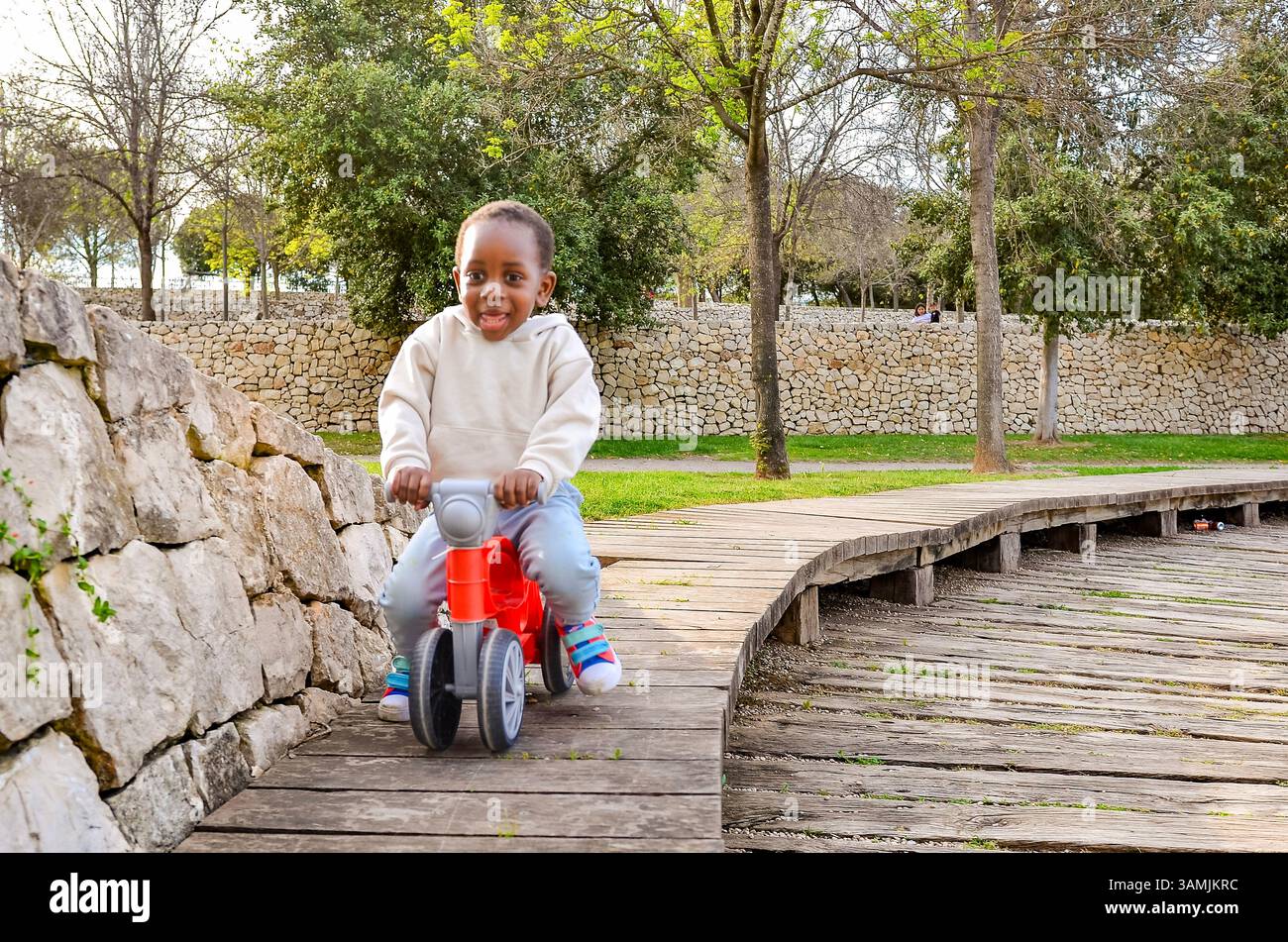 Enfant souriant appréciant de monter un vélo d'équilibre sur un chemin en bois dans un parc, favorisant le plaisir en plein air et le développement de la petite enfance Banque D'Images