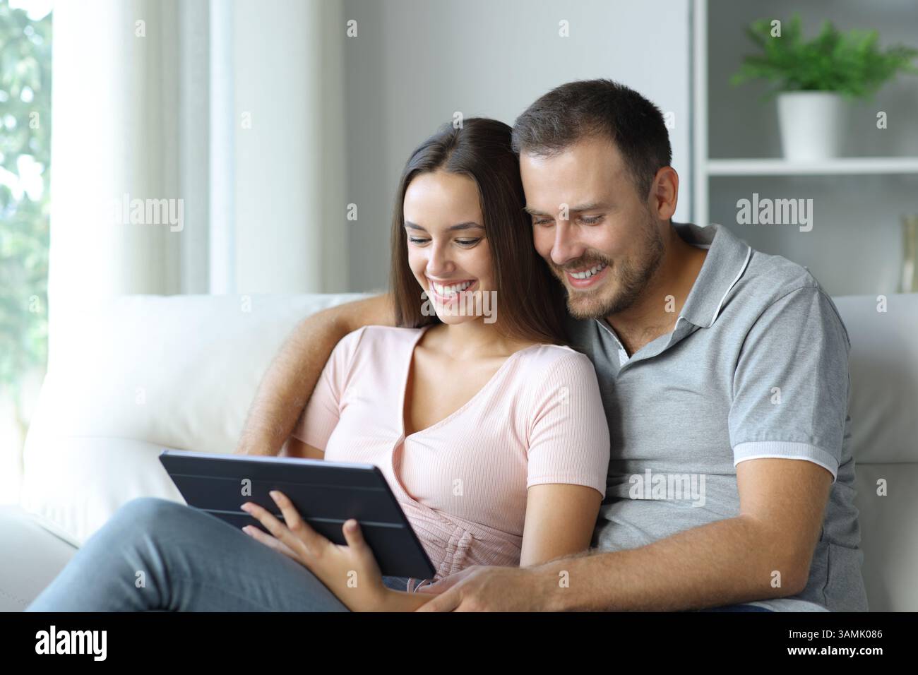 Heureux couple regardant les médias en ligne sur tablette assis sur un canapé à la maison Banque D'Images