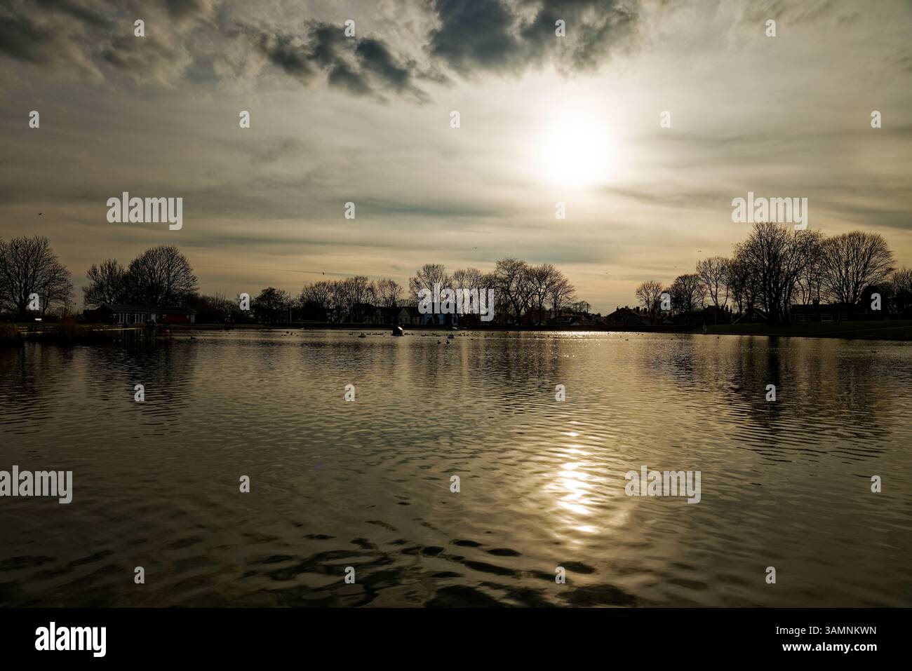 Le soleil couchant se reflète dans les eaux hivernales du Clarence Park Lido, Bury, Lancashire. Banque D'Images