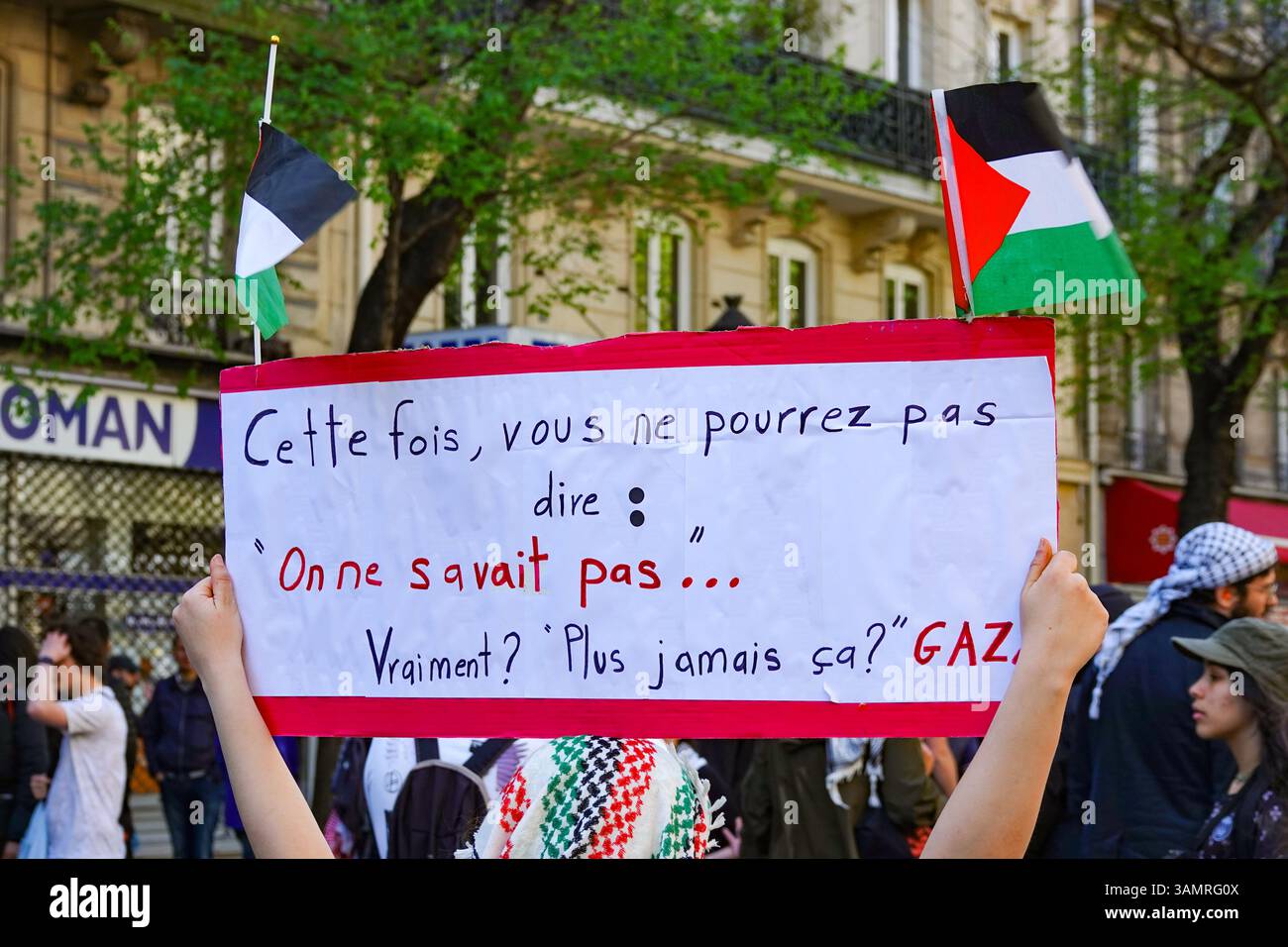 Un manifestant tient une pancarte avec un message contre le gouvernement et les politiciens en français lors d'un rassemblement pro-palestinien à Paris, avec des drapeaux palestiniens. Banque D'Images