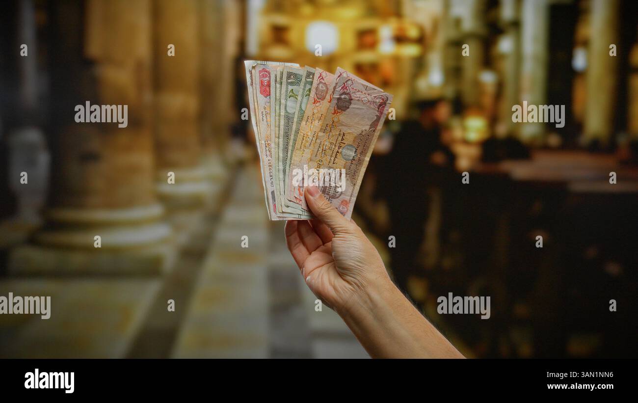 Homme tenant des dirhams des émirats arabes unis à l'intérieur avec l'intérieur de l'église en arrière-plan, mettant en vedette monnaie, argent, affaires, billets de banque, mise en évidence des aspects financiers dans Banque D'Images