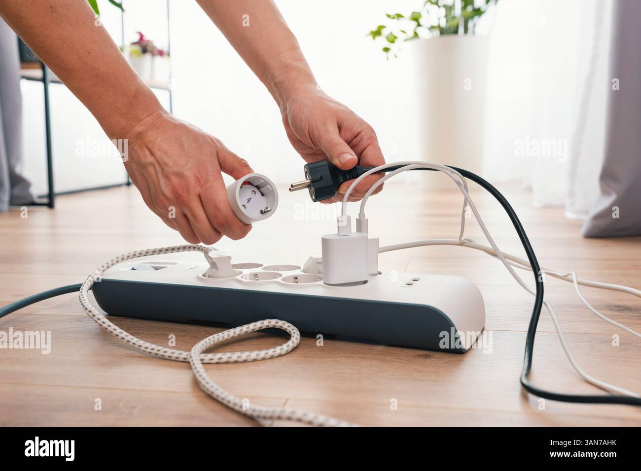 Homme utilisant une barrette d'alimentation avec plusieurs appareils électriques branchés Banque D'Images