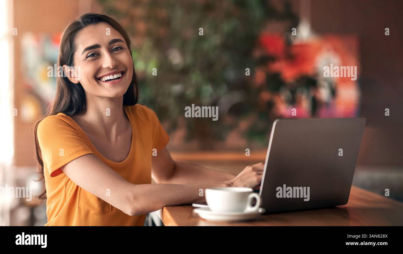 Une dame arabe joyeuse assise devant un ordinateur portable au café Banque D'Images
