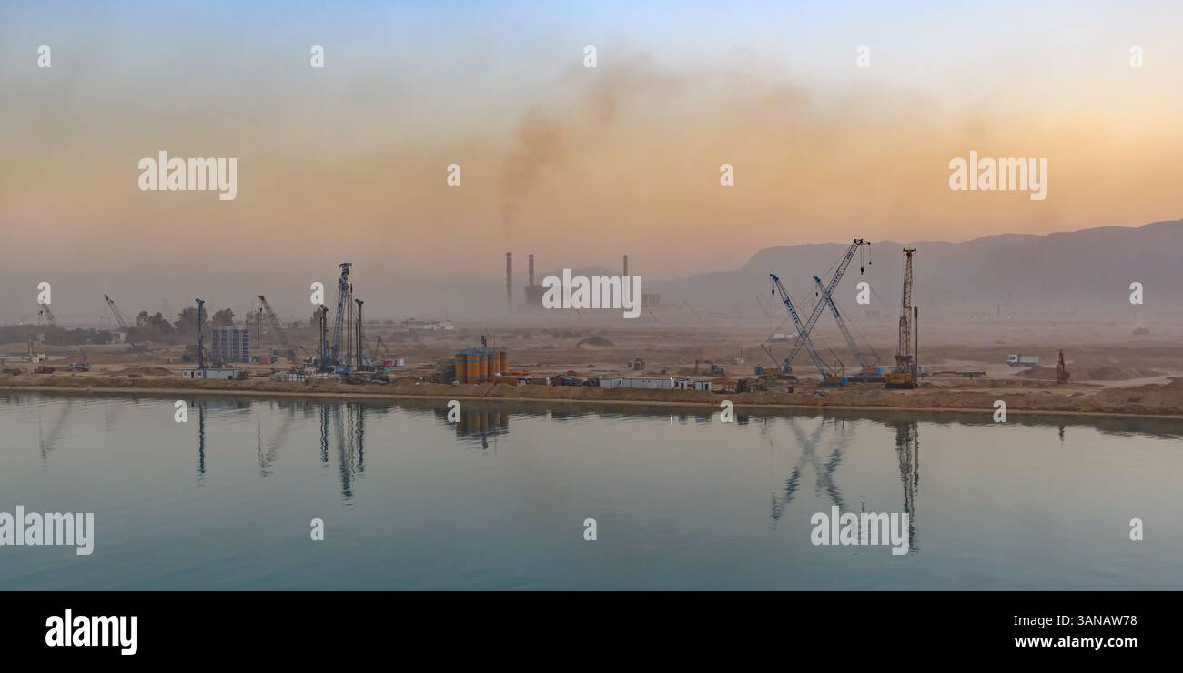 Sukhna, Egypte - 17 décembre 2022 : le paysage industriel est encadré par des grues et des cheminées, leurs silhouettes adoucies par un ciel brumeux, reflétant pro Banque D'Images