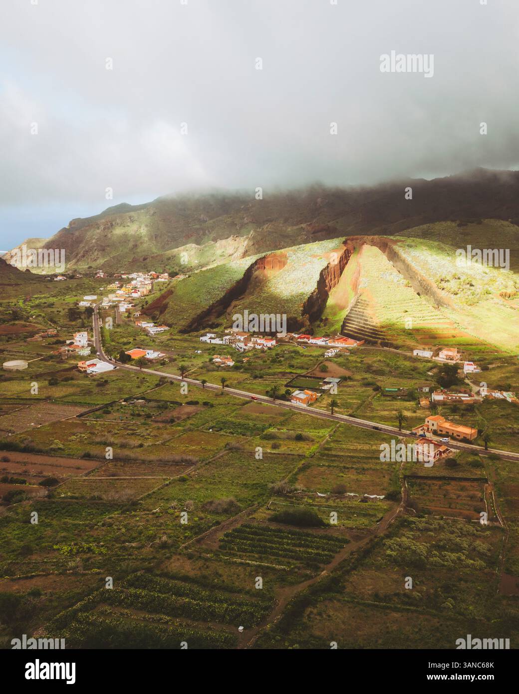 Vue aérienne des montagnes verdoyantes et des champs pittoresques avec un village tranquille sous un ciel nuageux, Buenavista del Norte, Espagne. Banque D'Images