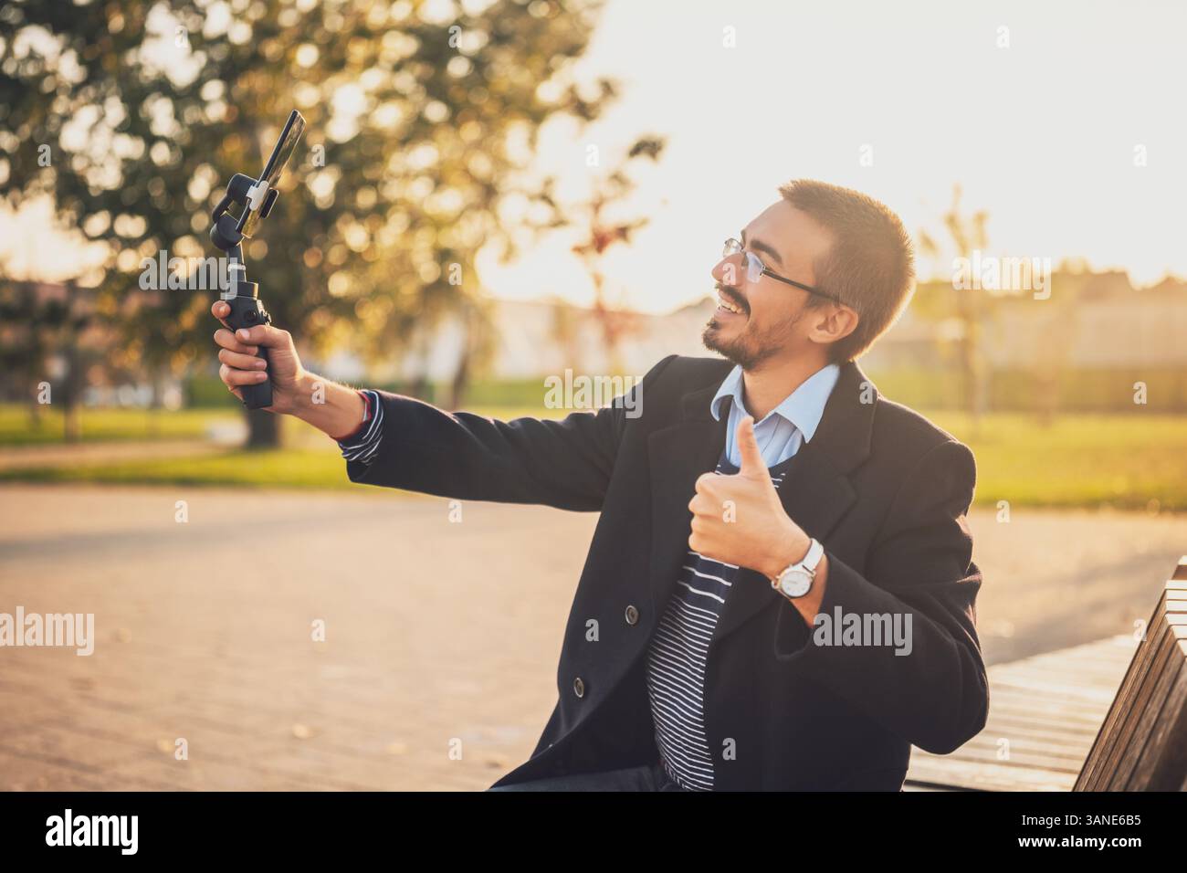 Entrepreneur masculin confiant montrant le pouce vers le haut tout en enregistrant un blog vidéo d'affaires avec stabilisateur de cardan en plein air. Banque D'Images