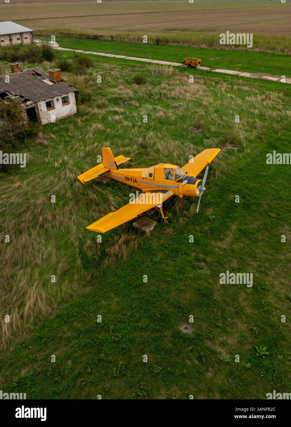 Vue aérienne d'un avion jaune abandonné sur une piste désaffectée entourée de champs d'herbe envahis par la végétation, Horne Oresany, Slovaquie. Banque D'Images