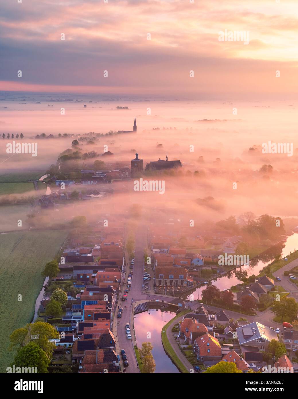 Vue aérienne d'une ville tranquille avec brouillard et nuages bas au lever du soleil, avec une charmante église et canal, Workum, Frise, pays-Bas. Banque D'Images