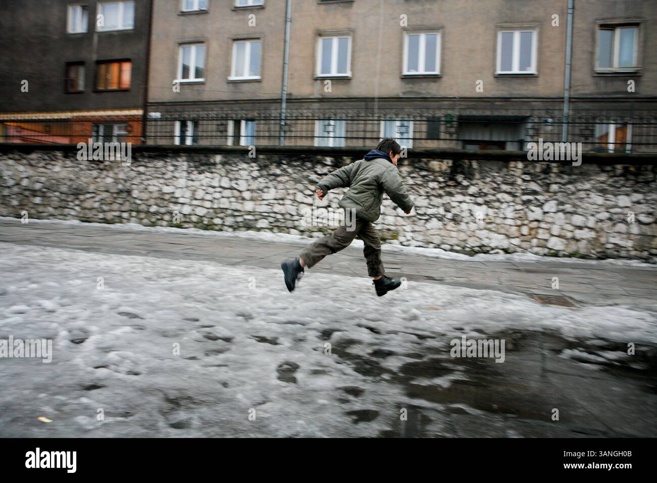 27 février 2010 - Cracovie, Pologne - Un garçon joue devant la cour de l'ancienne synagogue à Kazimerz. Avant la chute du communisme en Pologne, l’ancien quartier juif de Kazimerz à Cracovie était délabré et dangereux à visiter la nuit. Aujourd'hui, la région attire des milliers de touristes par an du monde entier. Le quartier était autrefois un centre animé de la vie juive avant d'être anéanti pendant la seconde Guerre mondiale. Les restaurants et cafés à thème juif servent une cuisine traditionnelle juive et polonaise et les synagogues restaurées contiennent des expositions détaillant la vie juive d'avant-guerre en Pologne. Une controverse existe sur un Banque D'Images