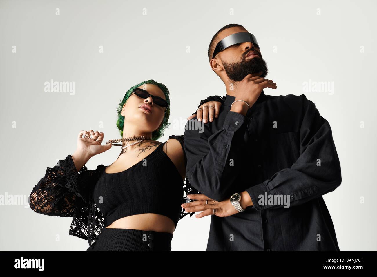 Couple se tient confiant dans le studio, portant des tenues élégantes et des lunettes de soleil, embrassant la diversité. Banque D'Images Couple se tient confiant dans le studio, portant des tenues élégantes et des lunettes de soleil, embrassant la diversité. Banque D'Images
